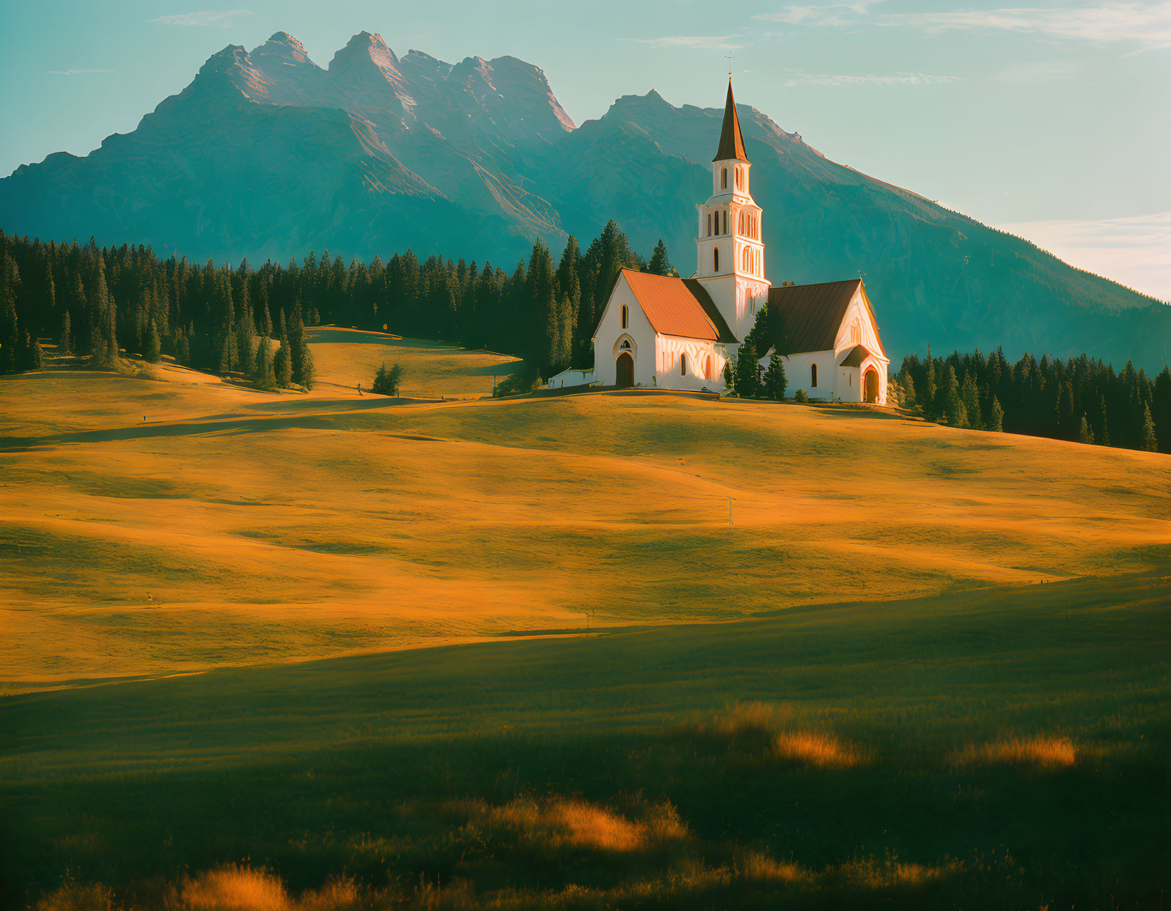 White church with tall steeple nestled among trees and mountains at sunset