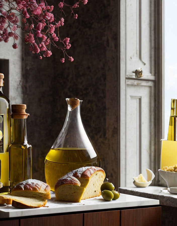 Kitchen counter still life with olive oil bottles, bread, olives, and pink flowers