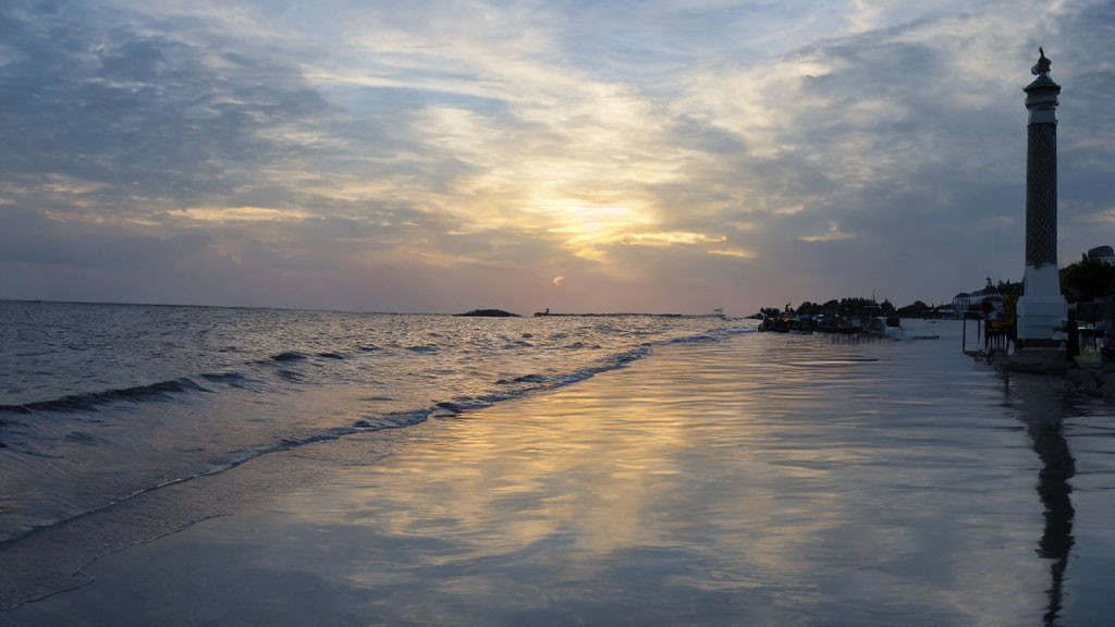 Tranquil beach sunset with reflections, minaret, and palm tree silhouettes