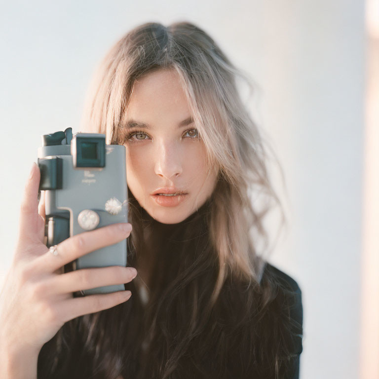 Serene woman with tousled hair holding camera in dreamy setting