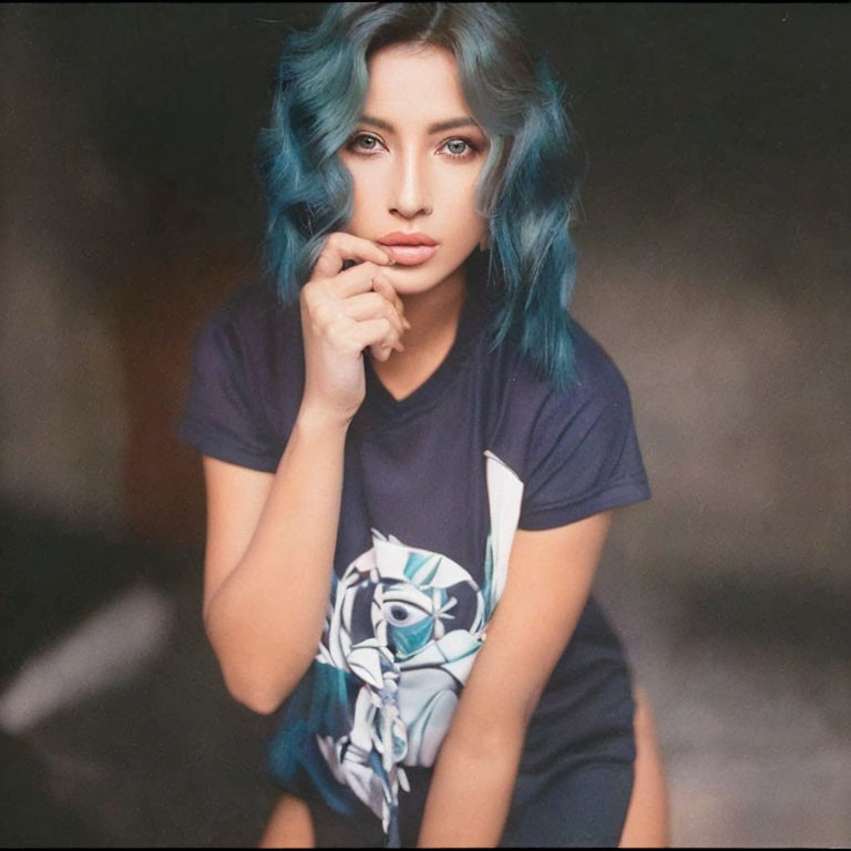 Blue-haired person in graphic t-shirt gazes at camera.