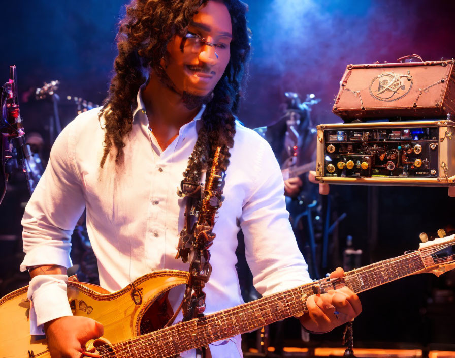 Smiling musician with curly hair and glasses on stage with guitar