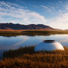 Tranquil landscape with reflective lake, golden grass, hills, blue sky, and futuristic structure