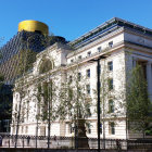 Modern building with traditional arches, blue sky, lush trees, and sunlight on facade