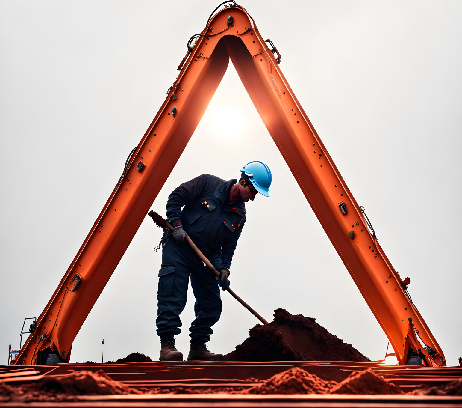 Construction worker in blue uniform shoveling soil between excavator arms