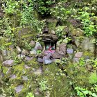 Tranquil Japanese garden with moss-covered stones, waterfall, lush greenery, and red-black pag