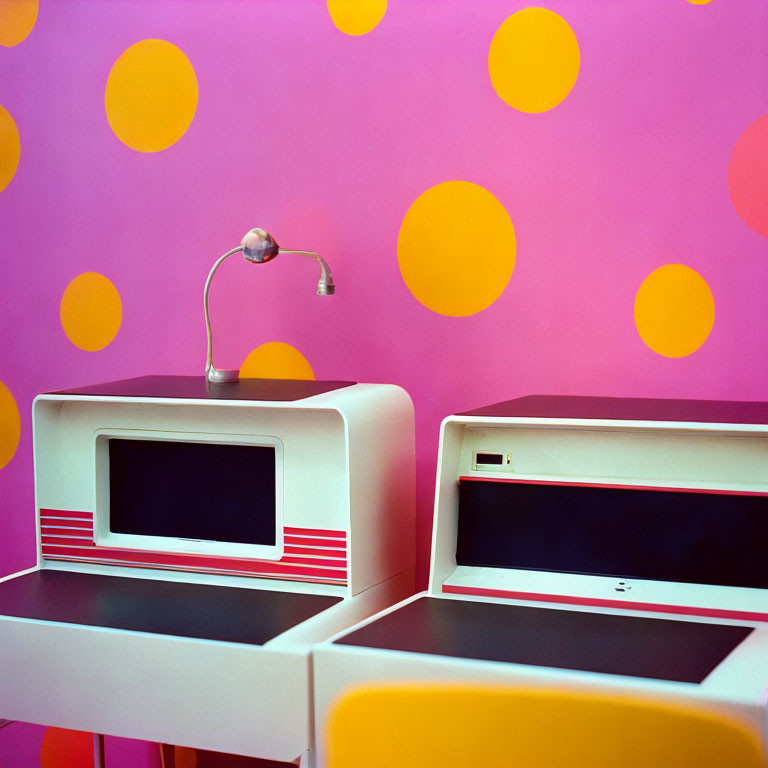 Vintage computers with red accents on desk against pink wall with yellow polka dots.