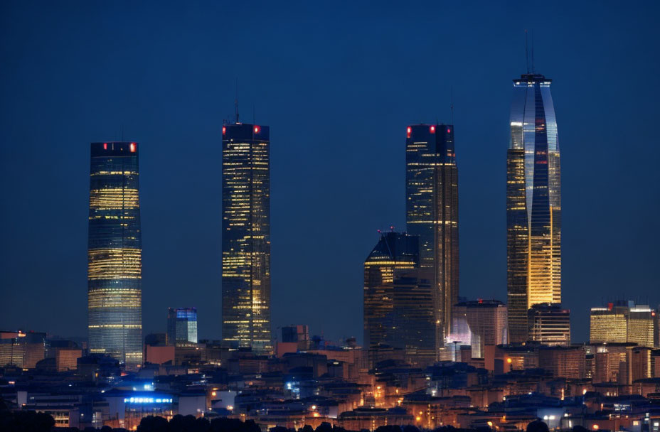 Nighttime cityscape with four illuminated skyscrapers against dusky blue sky