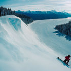 Person snowshoeing on snowy slope with forest and mountain range under clear blue sky