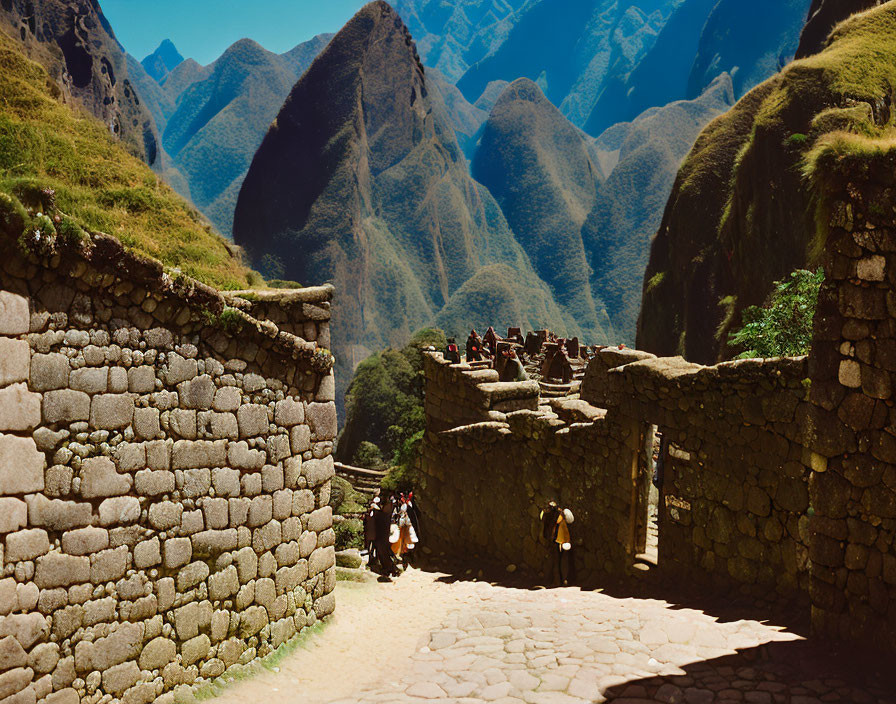 Ancient stone ruins of Machu Picchu with tourists, green mountain peaks, and clear blue sky