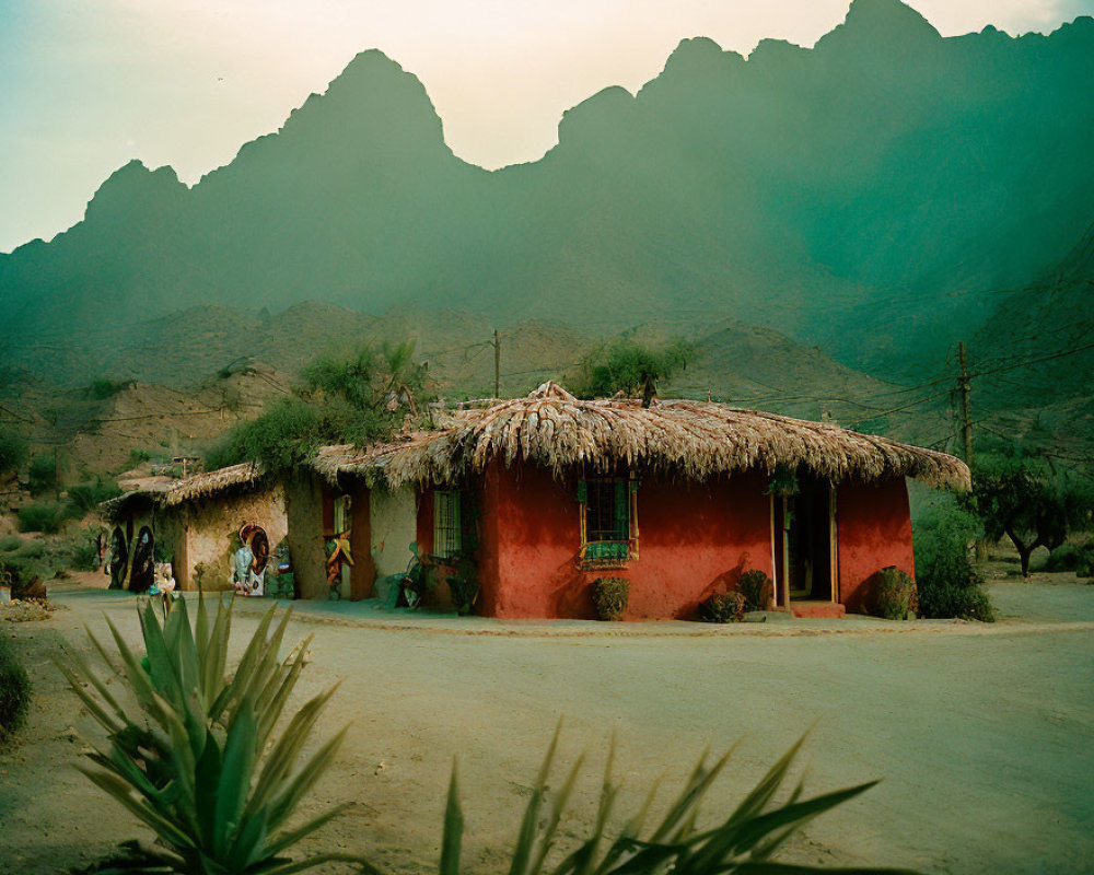 Traditional clay house with thatched roof in mountain backdrop at dusk