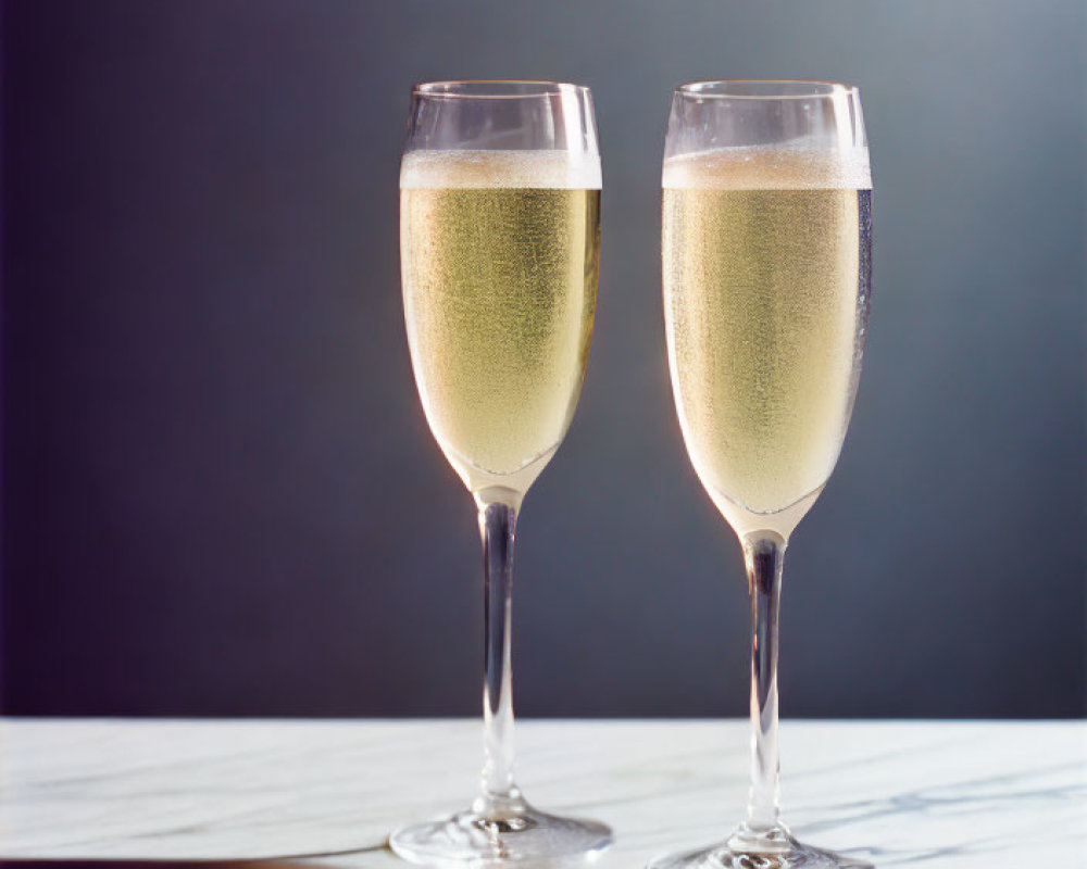 Sparkling champagne flutes on marble surface with dark background.