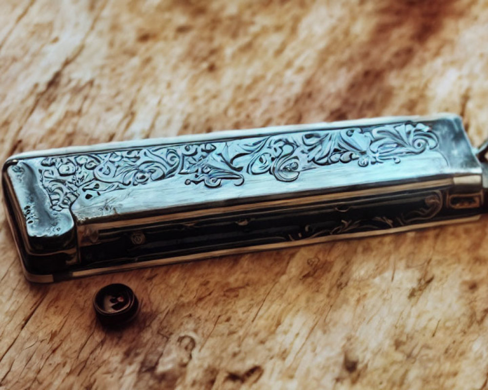 Silver harmonica with floral patterns on wooden surface next to black object