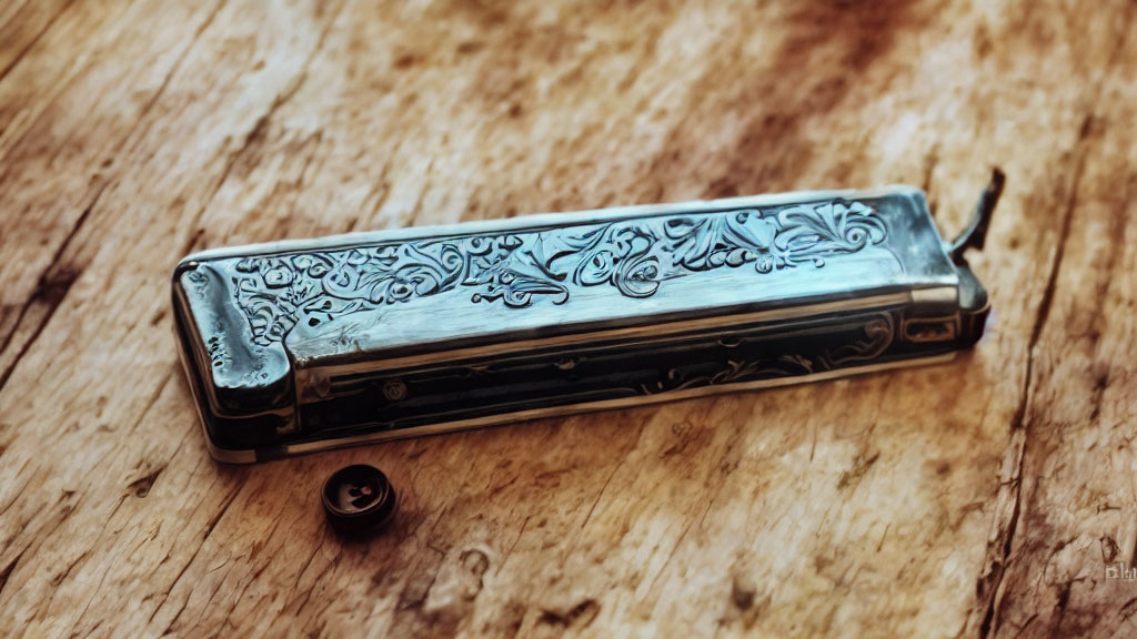 Silver harmonica with floral patterns on wooden surface next to black object