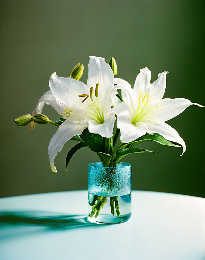 White Lilies in Blue Glass Vase on Table with Soft Green Background