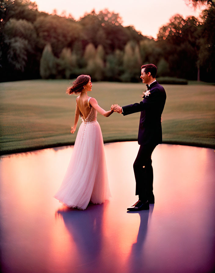 Formal attire couple holding hands at sunset by tranquil pond