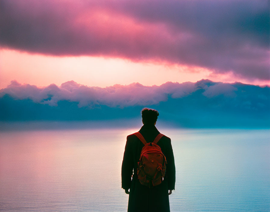 Person with backpack admiring vibrant pink and blue sky at dusk or dawn