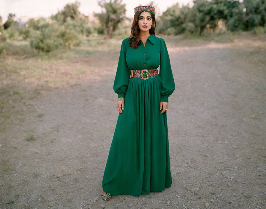 Woman in flowing green dress with embellished belt on dusty pathway.