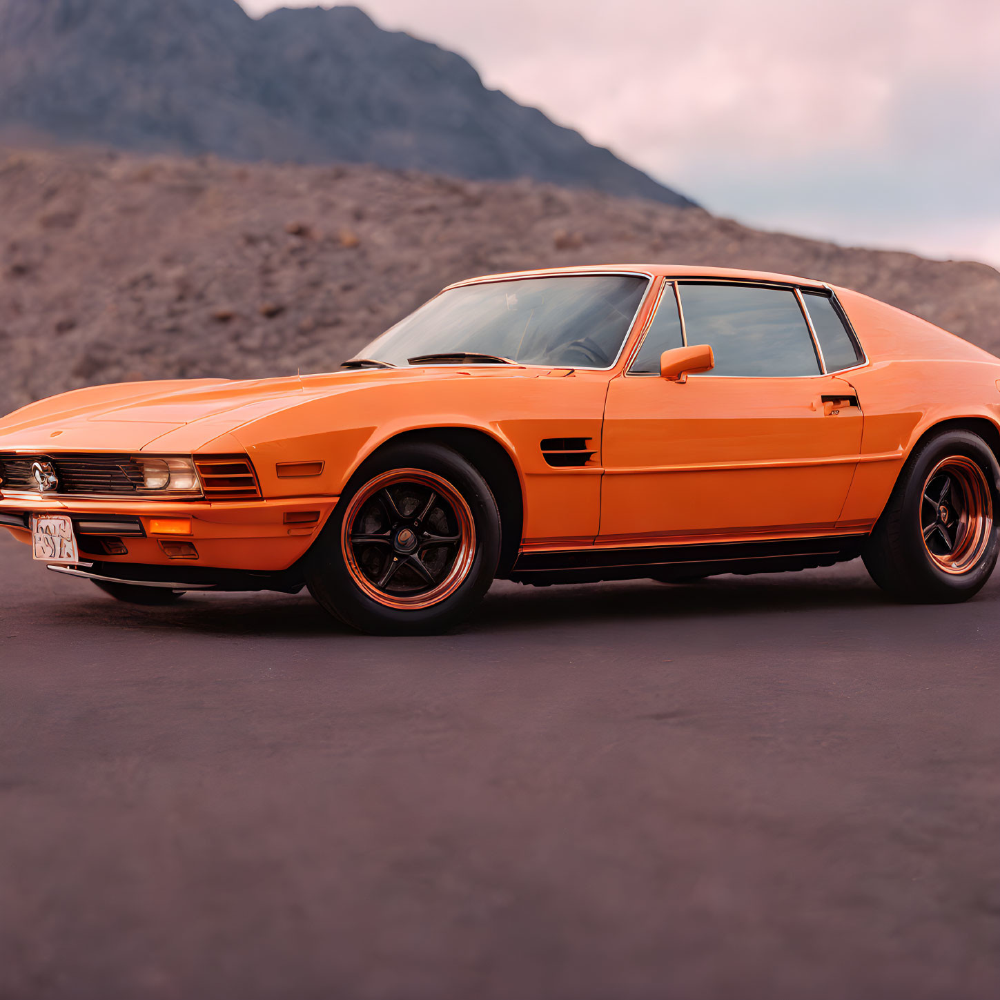 Orange Classic Car with Black Wheels on Asphalt Road with Mountain Background