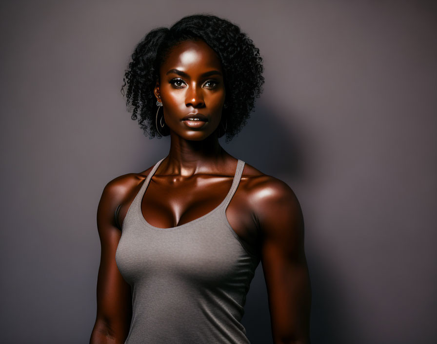 Curly-haired woman in grey tank top with radiant skin gazes at camera