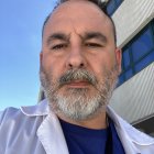 Bearded man in white suit jacket against blue sky and building.