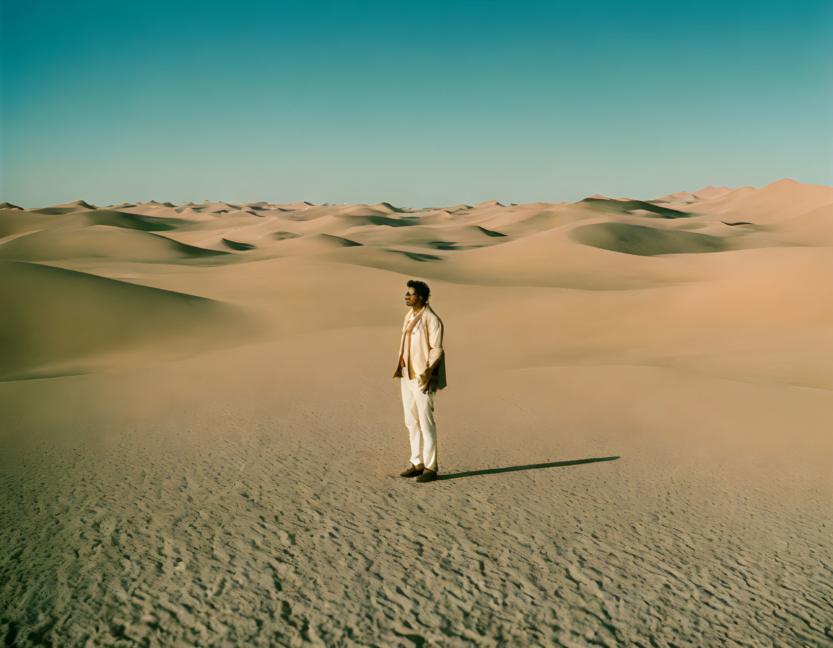 Solitary figure in light clothing amidst expansive desert dunes under clear sky