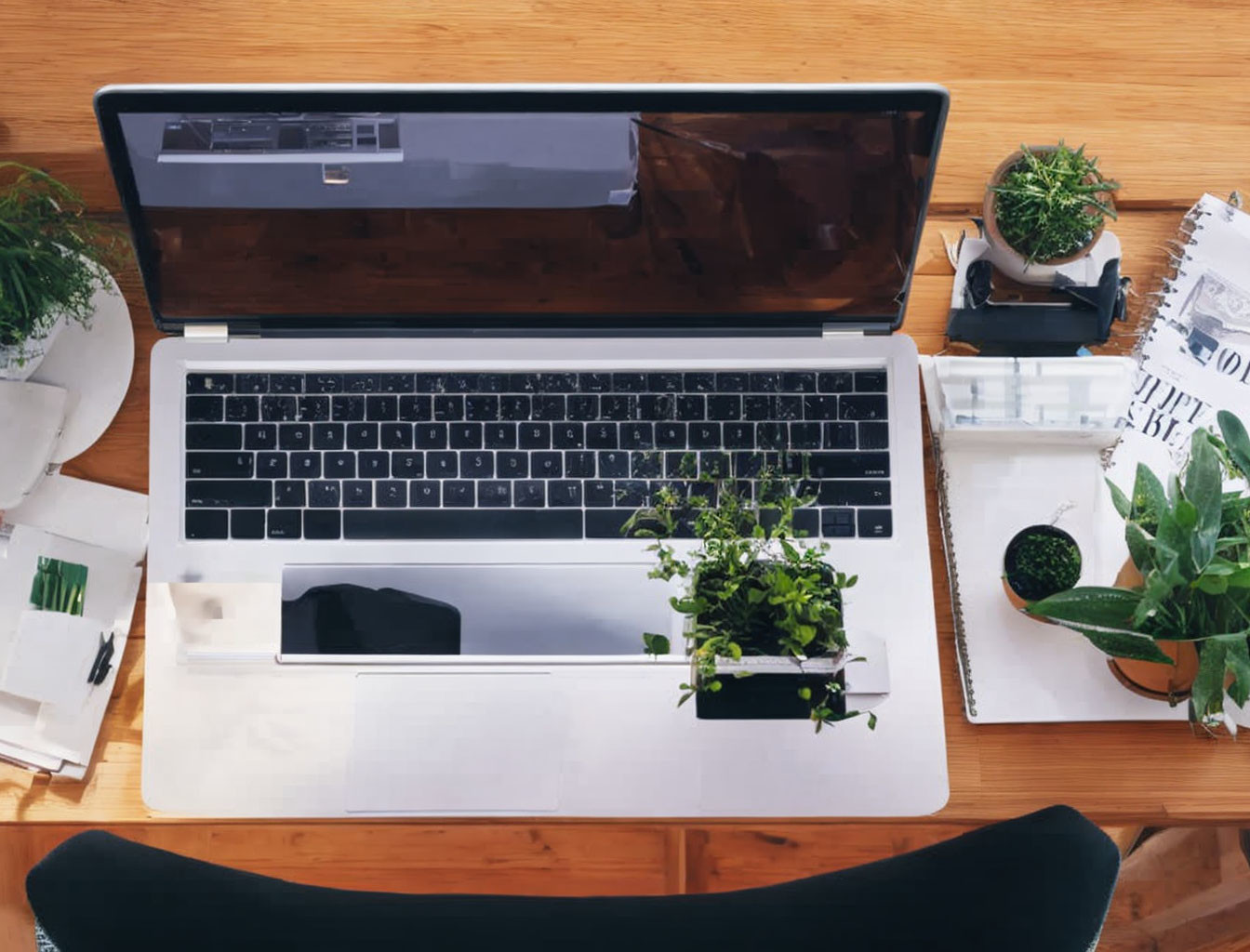 Laptop on wooden desk with plants, papers, and smartphone