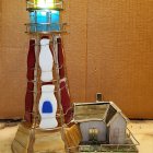 Whimsical ornate lighthouse with bright lantern and attached cottage in rocky surroundings