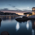 Tranquil coastal twilight scene with crescent moon, reflecting buildings and lights on calm water, and