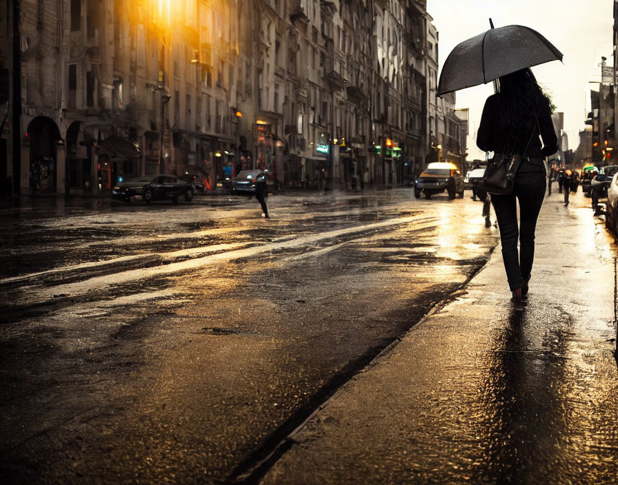 Person walking with umbrella on wet city street at sunset