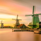 Dutch windmills by calm waterway at sunset