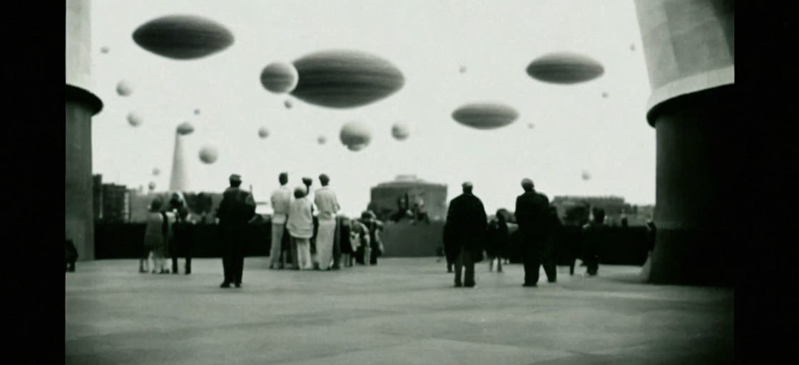 Vintage Black-and-White Photo of People on Terrace Watching Spherical Objects in Sky