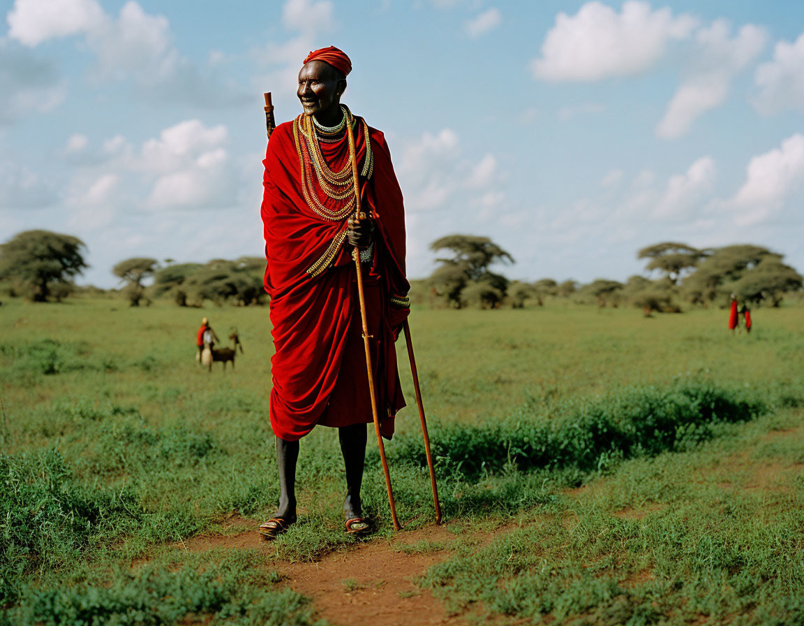 Traditional red attire person with staff in green field under blue sky