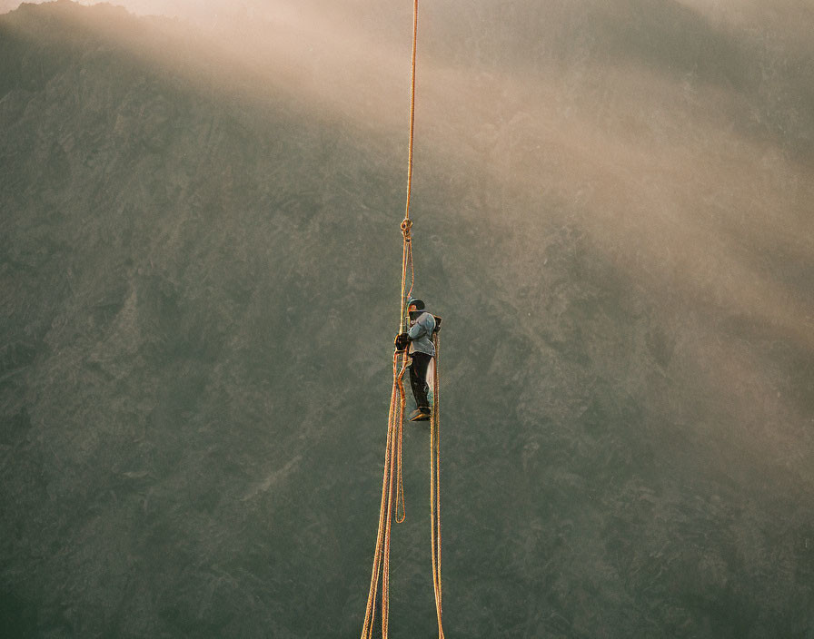 Climber rappelling down steep cliff in golden-lit mountain landscape