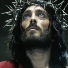 Man with Long Hair and Crown of Thorns in Solemn Pose on Dark Background