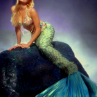 Mermaid costume with blue tail and pearl accessories on rock against cloudy sky