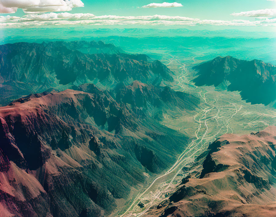 Rugged mountains, deep valleys, winding river, and hazy blue sky landscape.