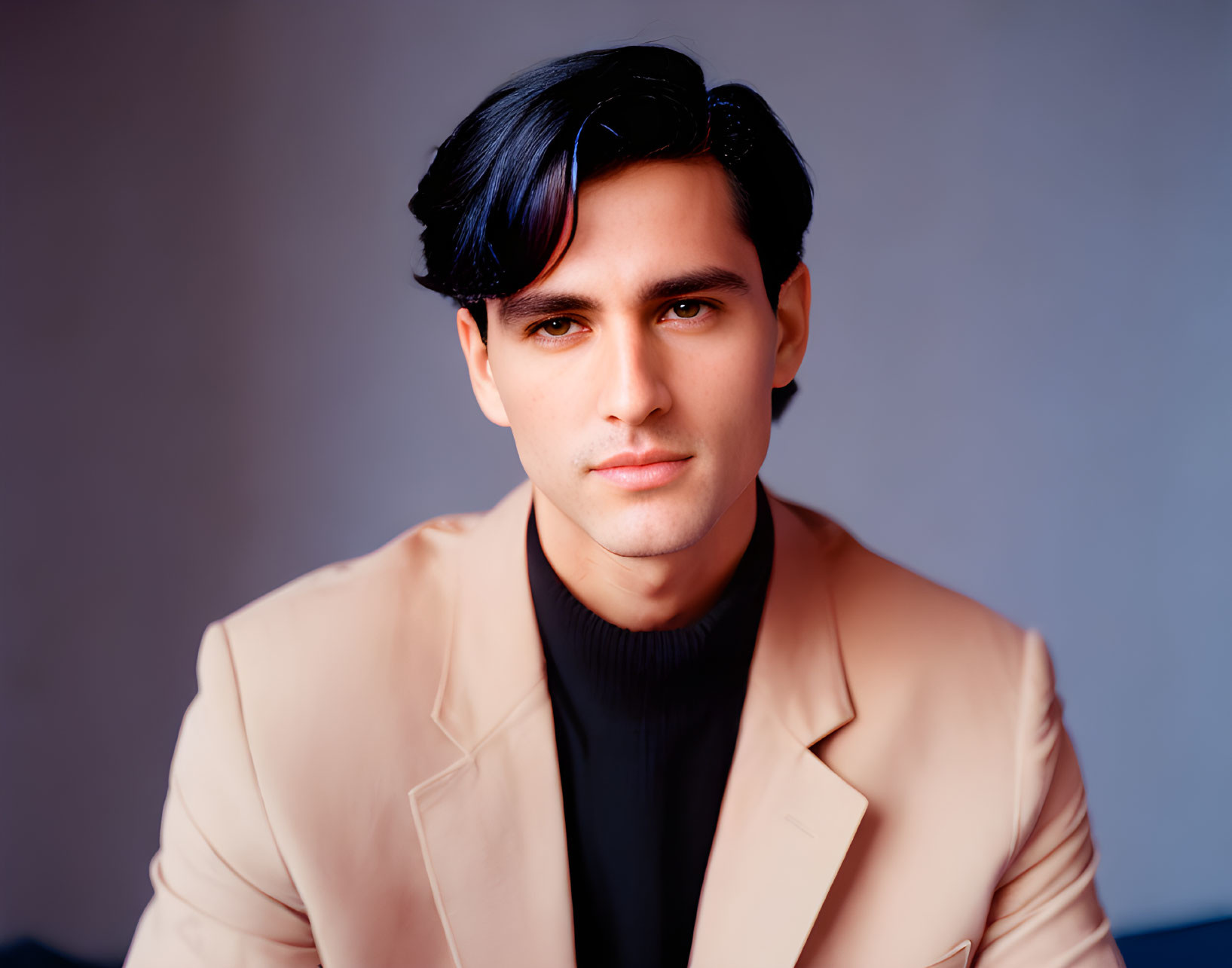 Dark-haired man in beige blazer and black turtleneck on blue background