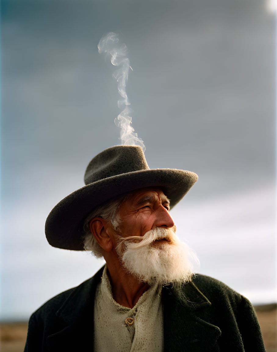 Elderly man with white beard exhales smoke under cloudy sky.