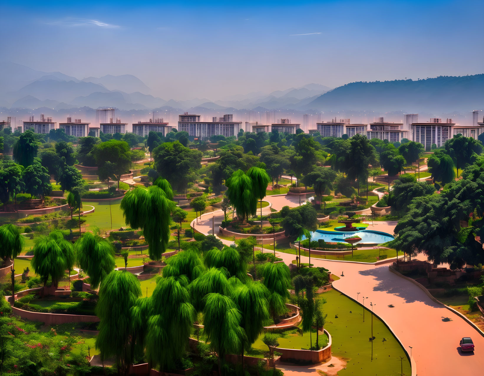 Serene park with pathways, trees, gardens, mountains, and cityscape under blue sky