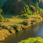 Scenic landscape: green fields, winding river, cliffs, and sunny path