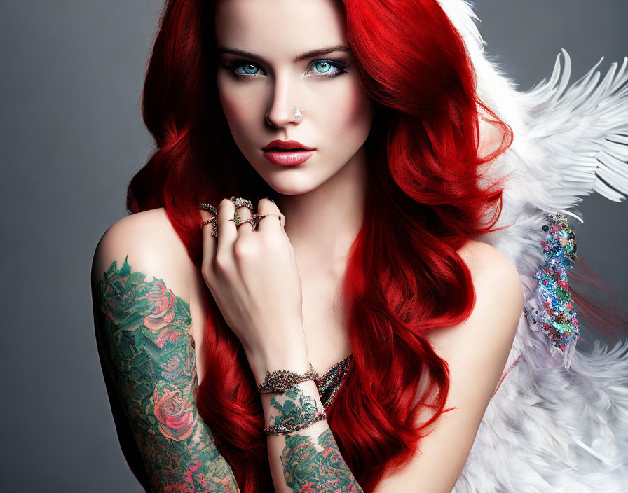 Vibrant red-haired woman with blue eyes, tattoos, and feathered wing pose.