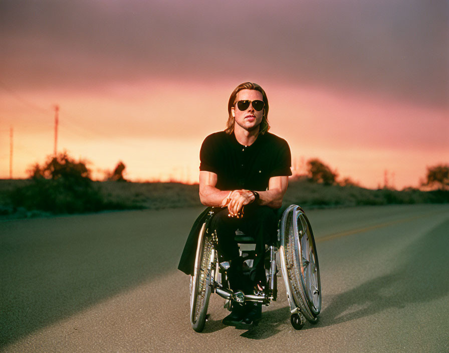 Sunset scene: man in wheelchair on empty road under colorful sky.