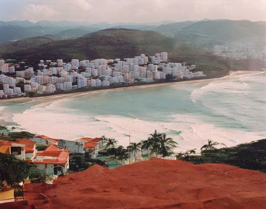 Densely packed white buildings in coastal cityscape with green hills and cloudy sky