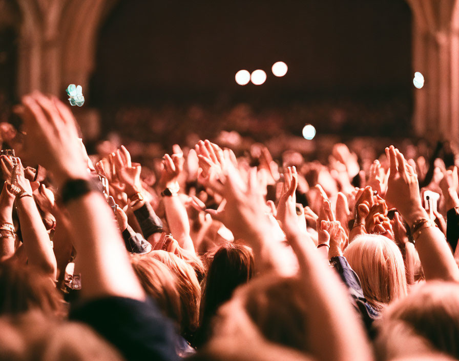 Crowd with Raised Hands at Event with Warm Lighting