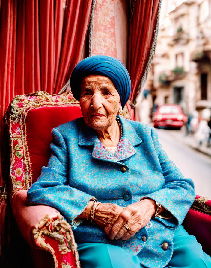 Elderly woman in blue headscarf on red chair in urban setting