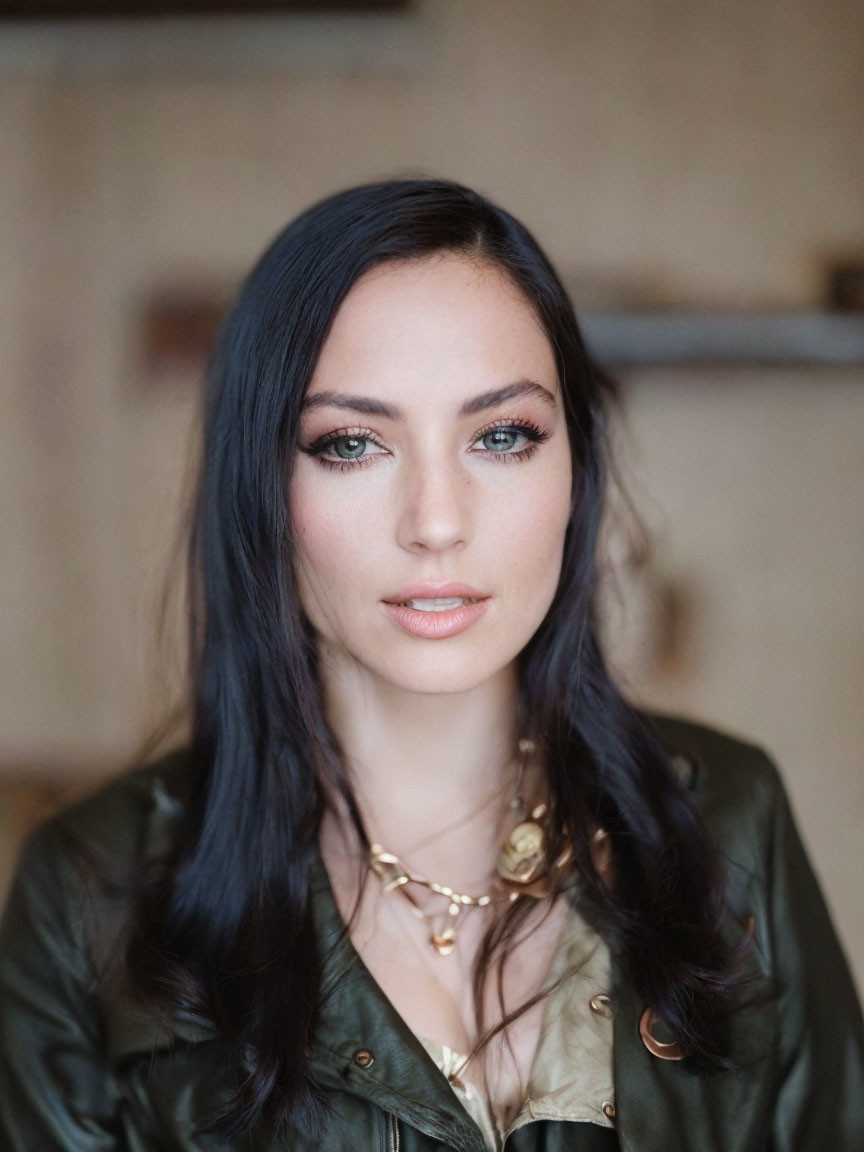 Dark-haired woman in green jacket and gold necklace with blue eyes