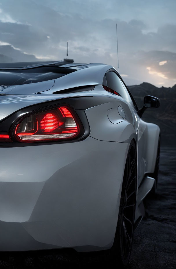 Silver Sports Car with Unique Tail Lights Parked Against Dusk Sky and Mountains