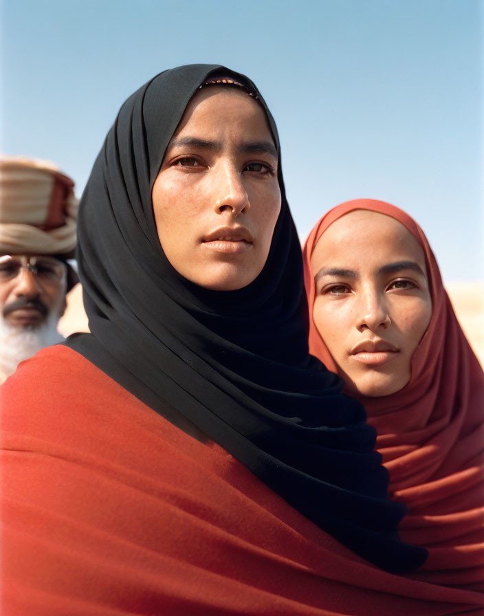 Women in hijabs and man in traditional headgear under blue sky