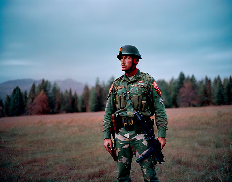 Uniformed soldier with rifle in grassy field at dusk